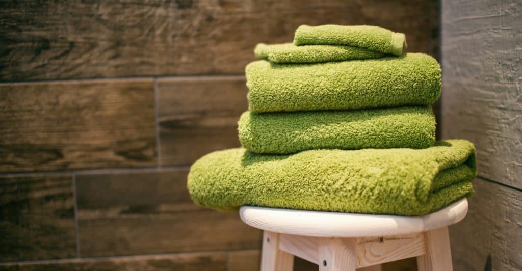 Stacked green towels on a small wooden stool against a wood-paneled wall.