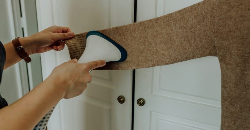  Hands holding a handheld steamer to a brown sweater sleeve.
