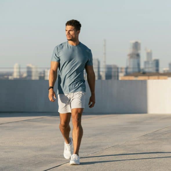 A muscular man on the roof of a building wearing a fitted t-shirt with fitted shorts.