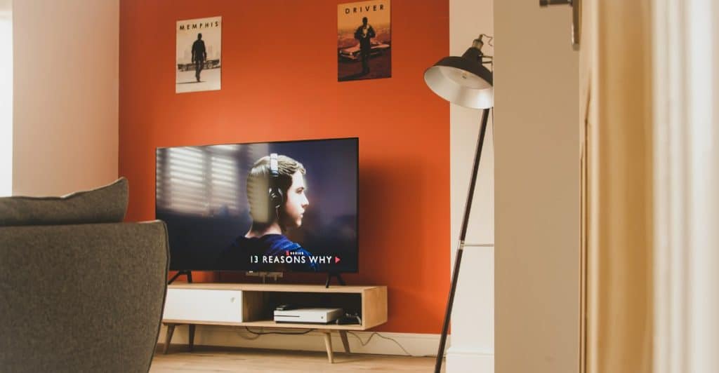 A TV  placed in a living room setting, displaying the series "13 Reasons Why".