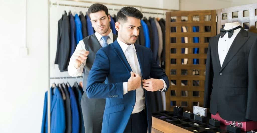 A tailor adjusting the suit jacket on a man in a tailor shop.