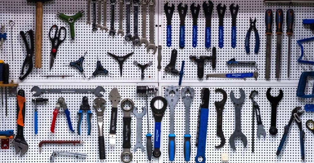 A white pegboard wall displaying a wide variety of neatly organized hand tools, including wrenches, pliers, and screwdrivers.