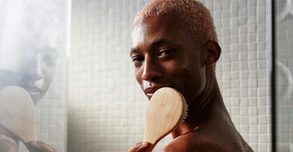 A person holding a wooden back scrubber in the shower.
