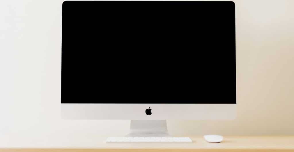 A white computer screen, keyboard, and mouse on a light wooden desk.