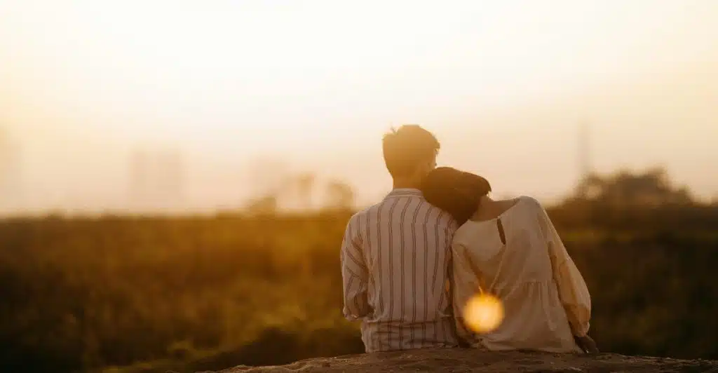 A woman resting her head on her partner's shoulder facing a field.