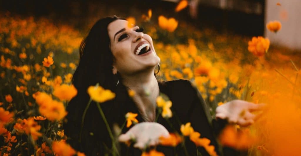 A woman with dark hair laughing and reaching out in a field filled with orange flowers.