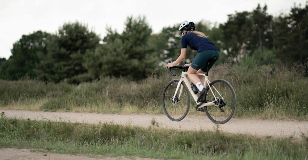 A woman riding a bicycle on a dirt path through a grassy field.