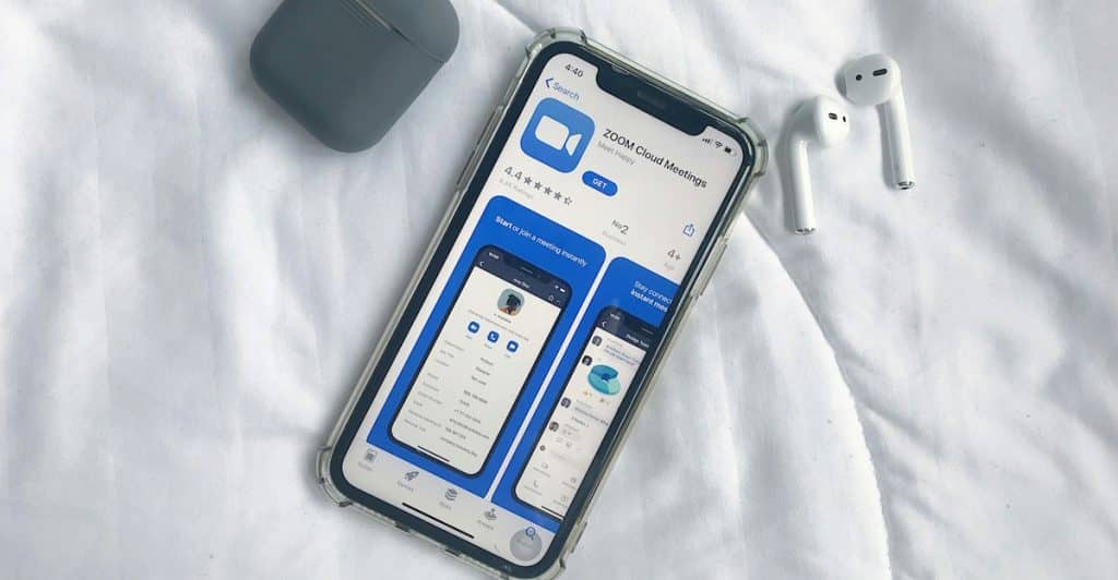 A smartphone and earbuds arranged on a white textured surface, with the Zoom app visible on the phone's screen.