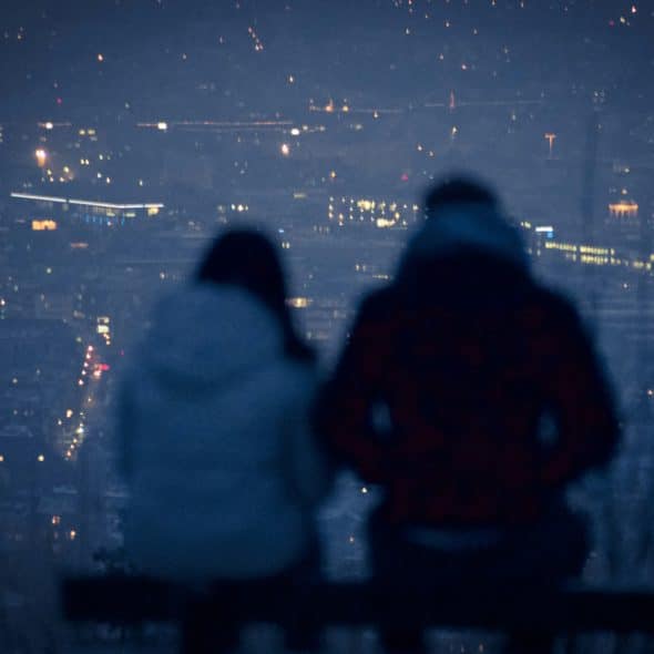 Two people sitting on a bench overlooking a city at night.