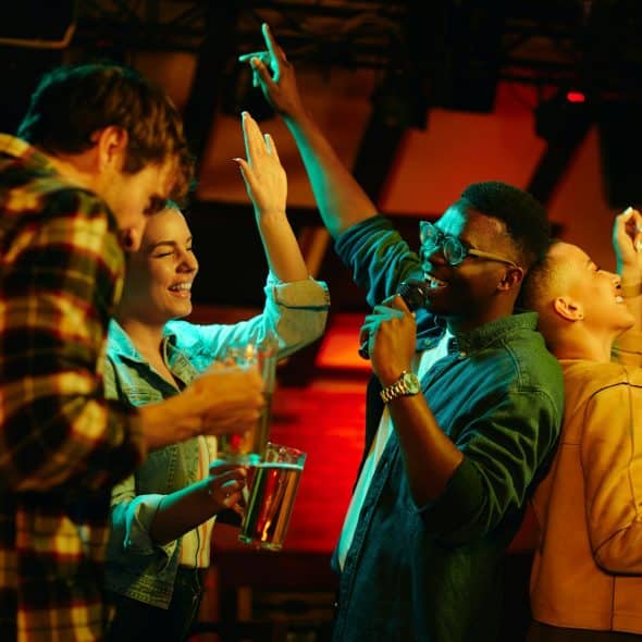 A diverse group of friends singing karaoke with drinks.