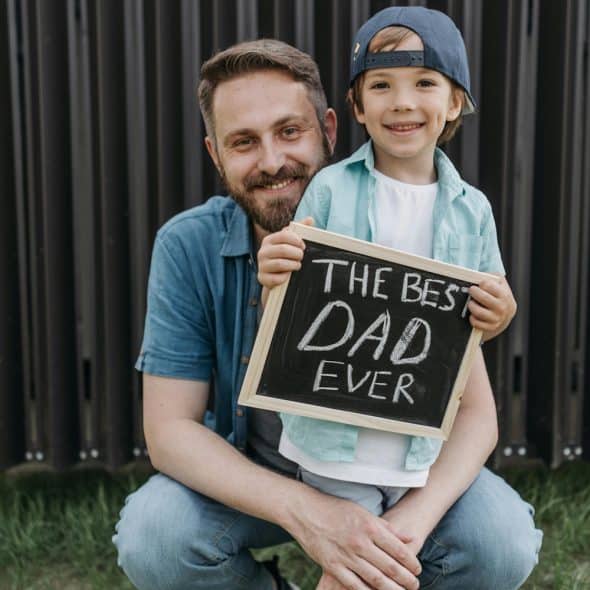 A father and son are crouching down, with the son holding a sign that says "THE BEST DAD EVER"