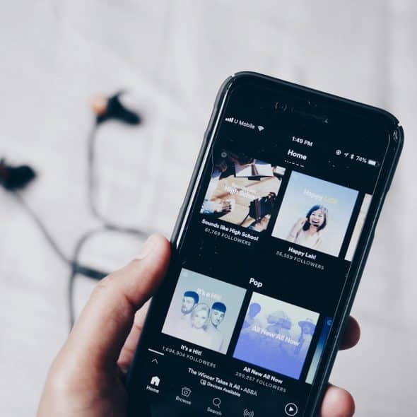 A hand holding a black smartphone displaying a music streaming application with various playlists and songs visible on the screen.