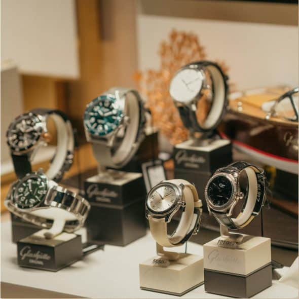 A collection of luxury watches displayed in a store, with some on stands and one next to a decorative boat model.