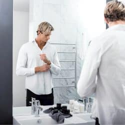 A man checking his appearance in a mirror with grooming products on the counter.