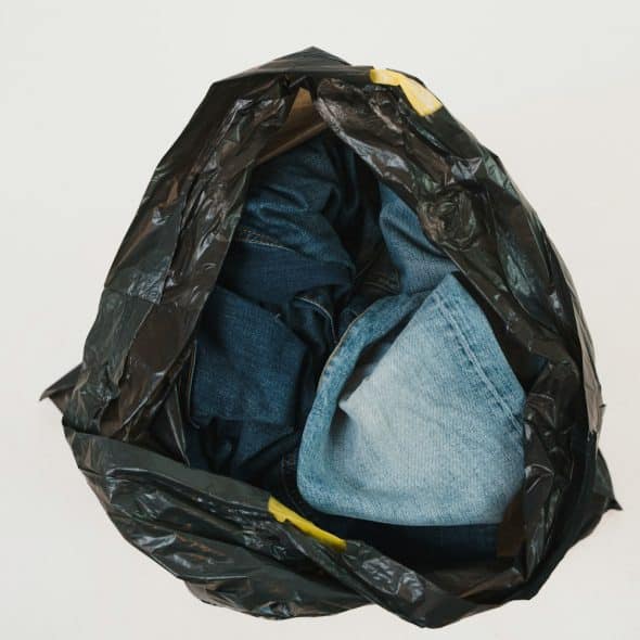 A black garbage bag is filled with blue denim jeans and jackets, with some yellow accents visible on the bag.