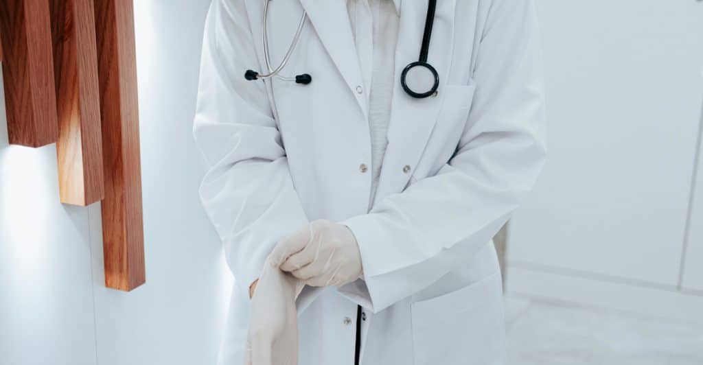 The torso of a person in a white doctor's coat and stethoscope putting on white.