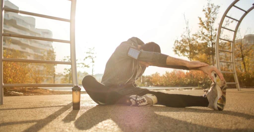 A man stretches post-workout in the park with the sun on his back.
