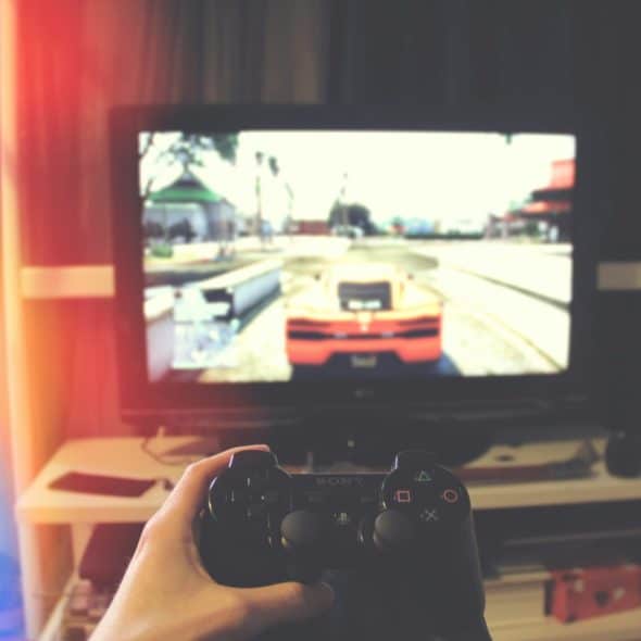 A person holding a black game controller while playing a racing video game on a large screen television.