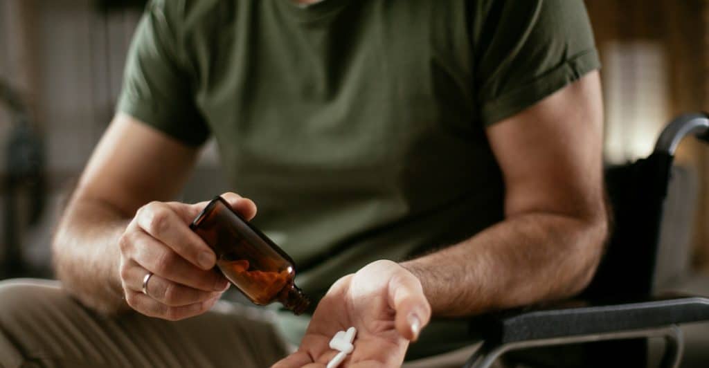 A person's hands pouring three capsules from a brown pill bottle into their palm.