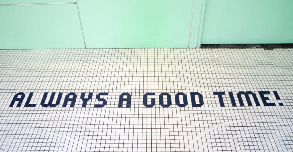 The phrase "ALWAYS A GOOD TIME!" written in black capital letters on a white tiled floor.