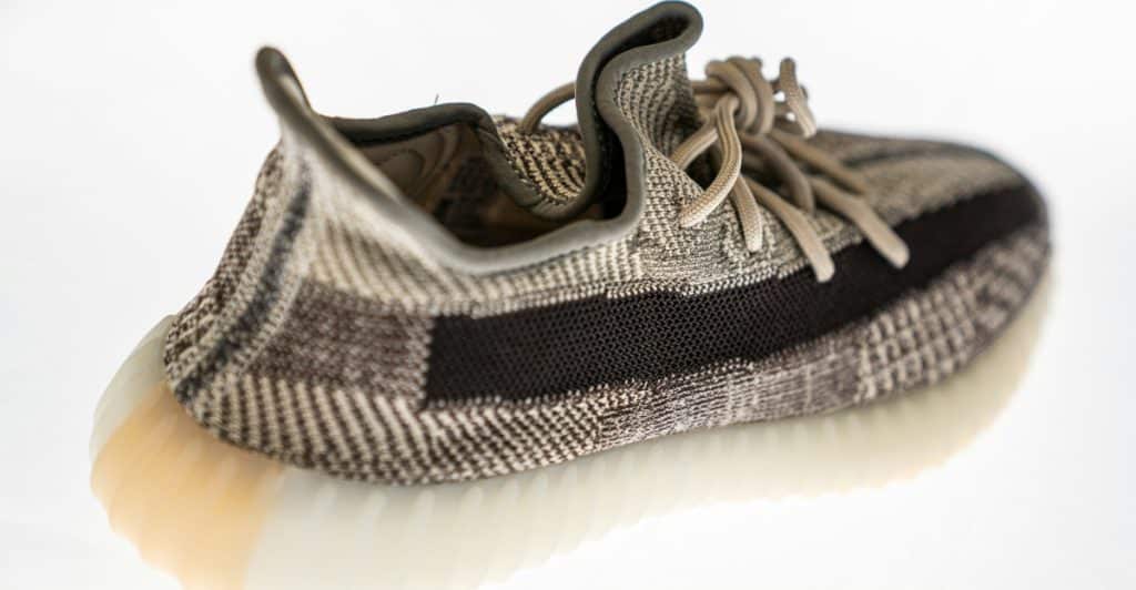 A grey, black, and tan Adidas Yeezy Boost 350 V2 sneaker viewed from an elevated angle on a white surface.