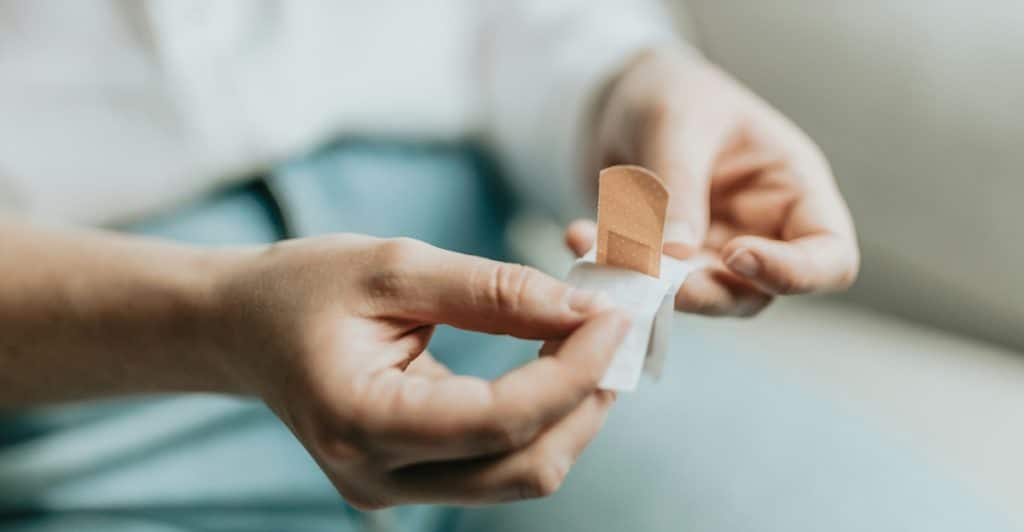 Hands peeling a bandage to apply to skin.