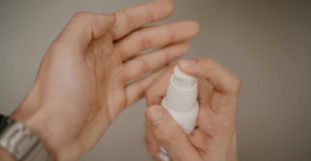 Hand applying ointment from a white pump bottle.