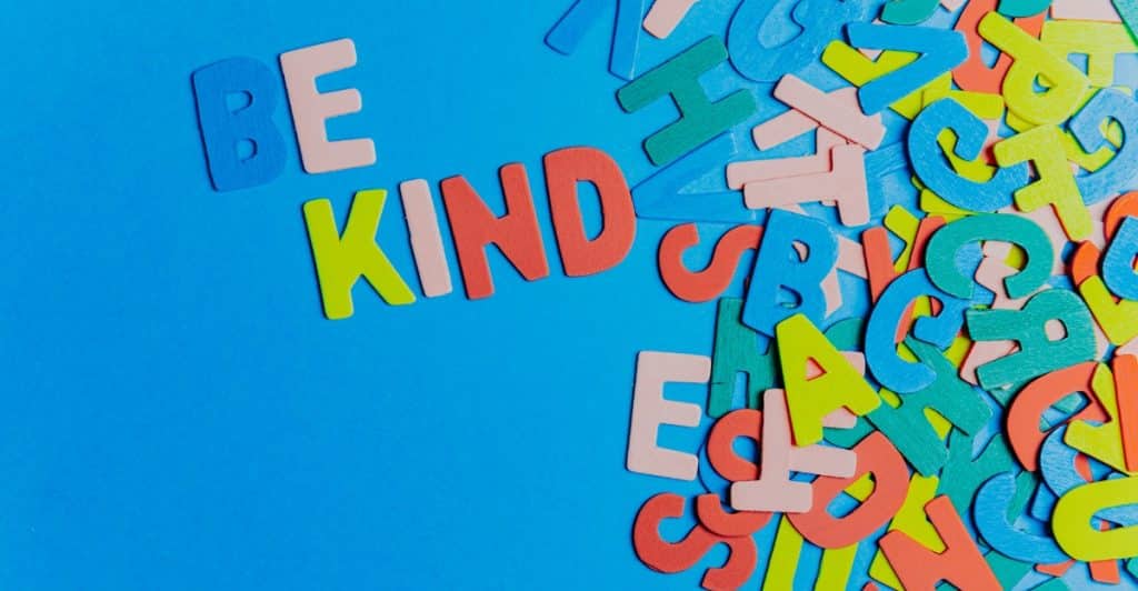 The phrase "BE KIND" spelled out with colorful block letters scattered on a blue background.