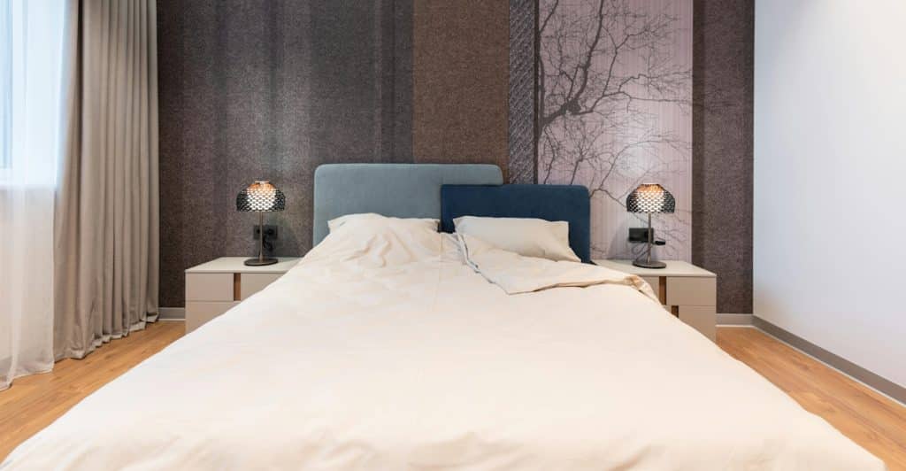 A bedroom is shown with a bed, two lamps on nightstands, and curtains.