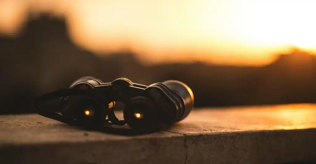 A pair of lightweight binoculars resting on a concrete surface, silhouetted against a warm sunset sky