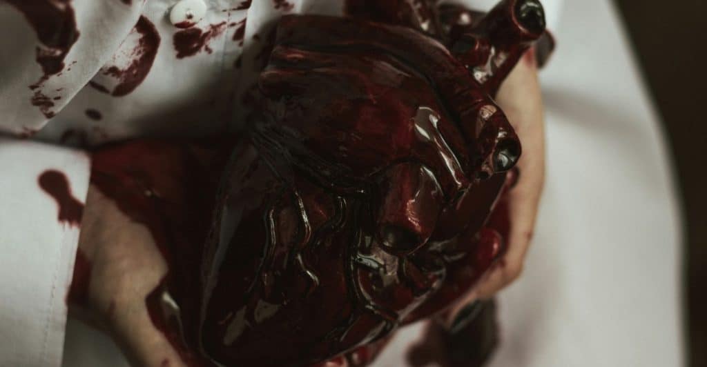 Hands holding a human heart covered with blood.