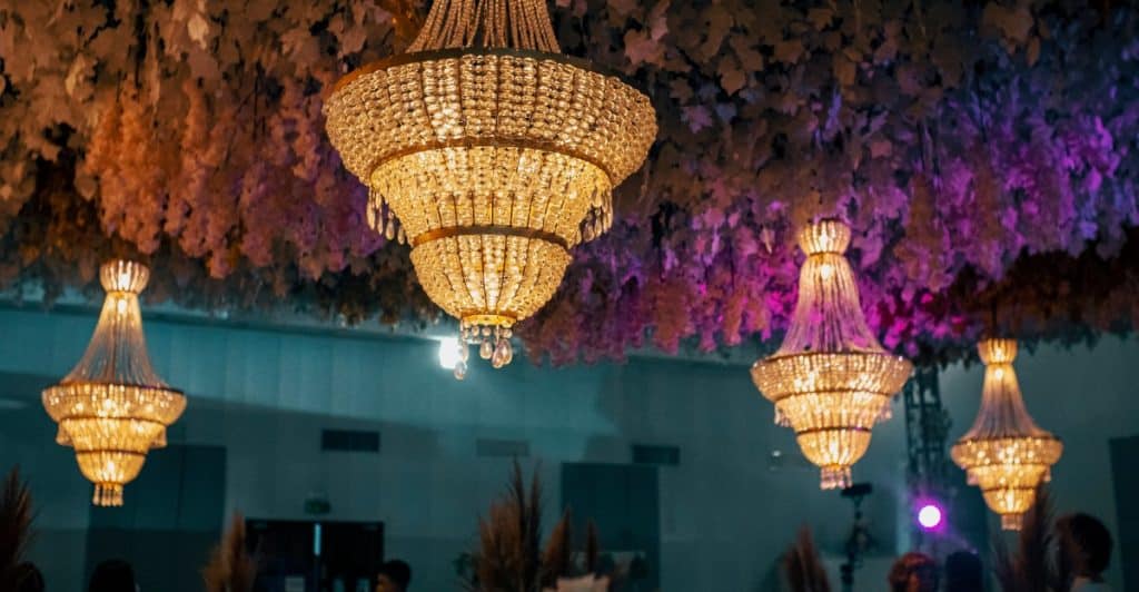 Multiple ornate chandeliers hanging from a ceiling adorned with greenery and lights.