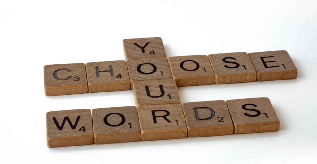 Wooden scrabble tiles arranged on a white surface to spell out "CHOOSE YOUR WORDS" in a crossword pattern.