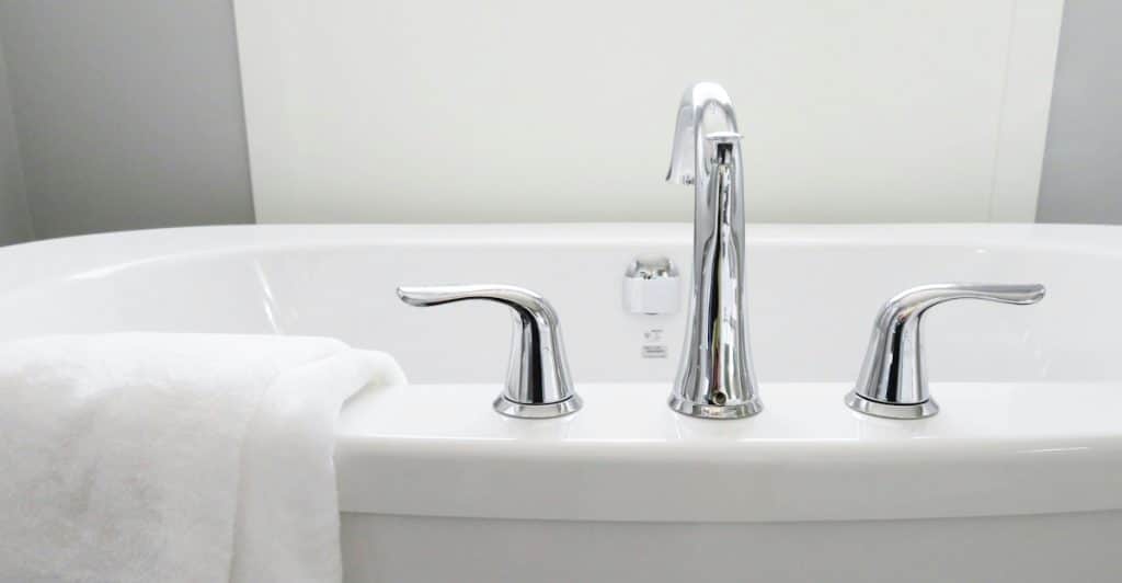 A clean white towel resting on the edge of a white bathtub with chrome fixtures.