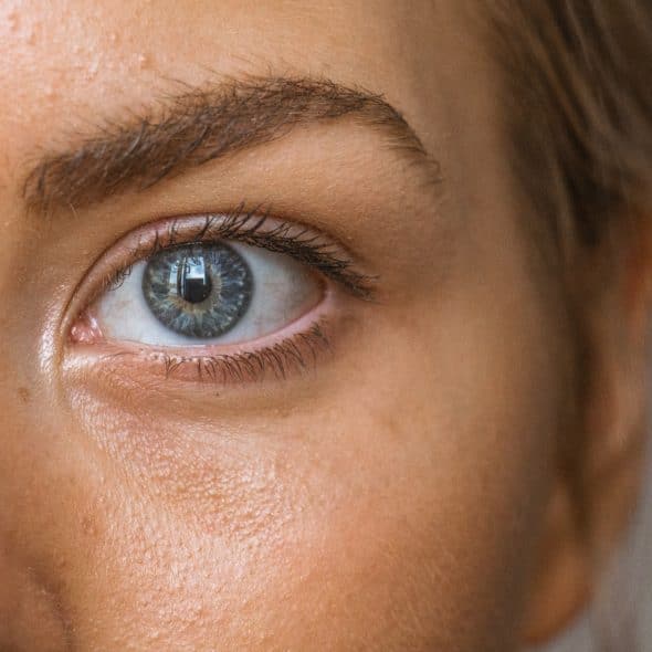 A close-up shot of a person's eye with a light blue iris and visible skin texture.