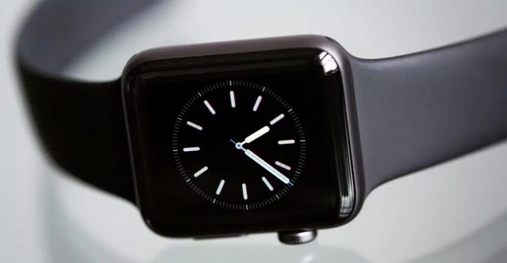 A close-up view of a black smartwatch displaying a minimalist analog clock face on a reflective surface