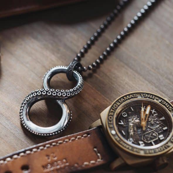 A close-up of a vintage watch, necklace, and knife on a wooden surface.