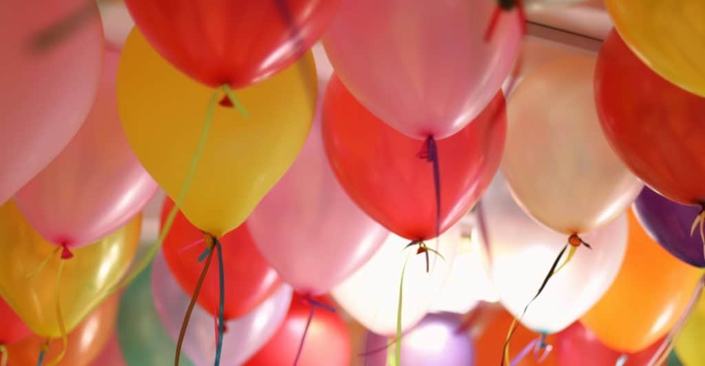 A cluster of colorful balloons filling the top of the frame, tied with ribbons.