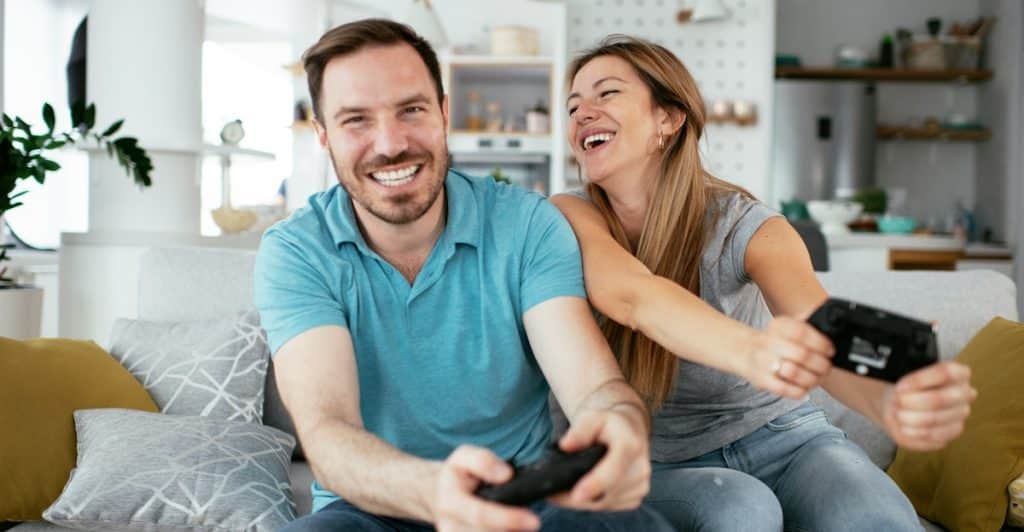 A couple laughing while playing video games on the couch.