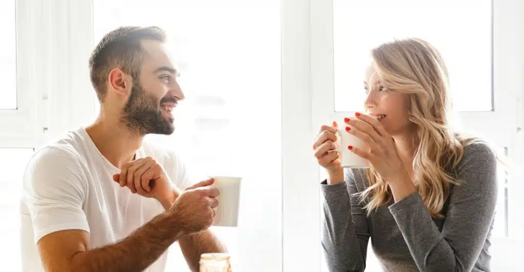 A smiling couple enjoying coffee together at a breakfast table with toast and jam.