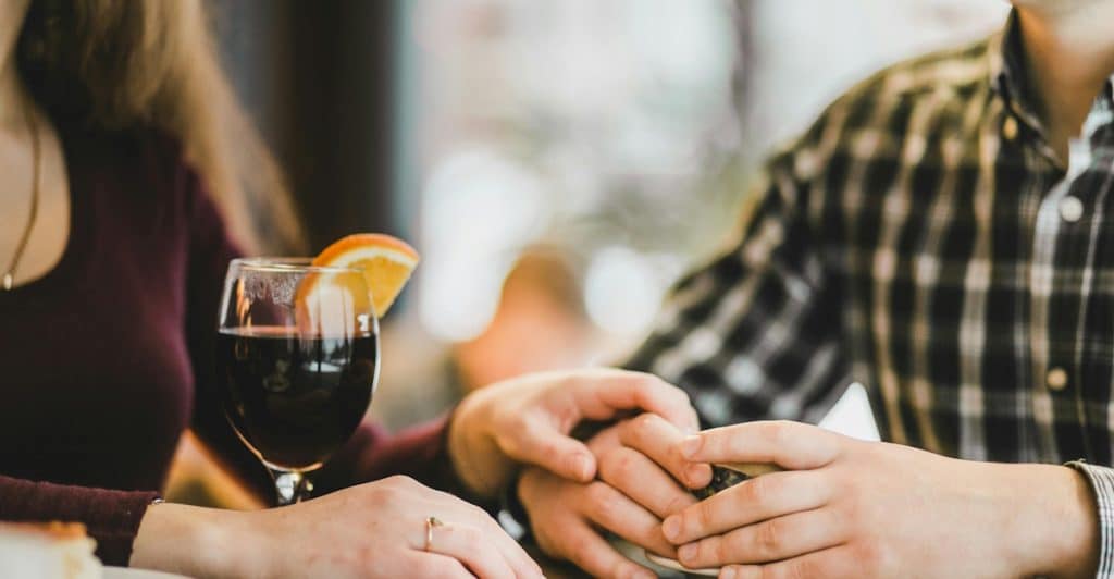 A man and a woman holding hands across a table with drinks and food.