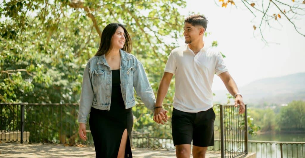 A man and a woman holding hands and smiling at each other while walking outdoors.