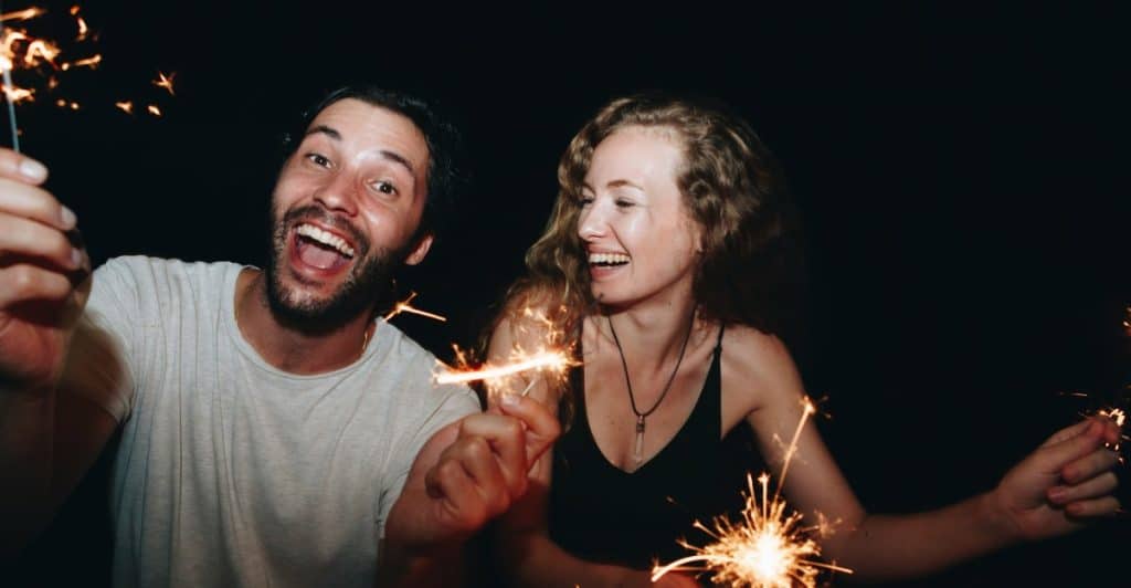 A man and a woman smiling and holding lit sparklers in the dark.