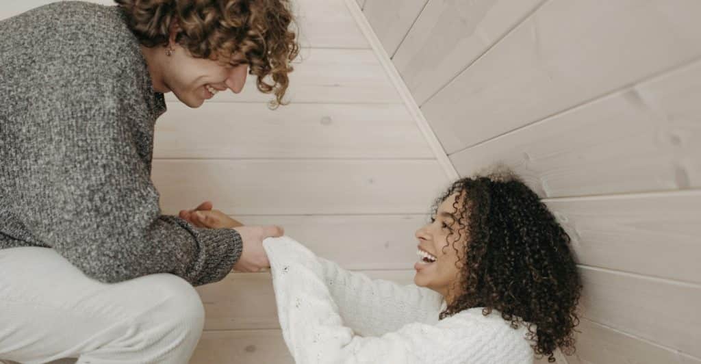 A man and a woman holding hands and laughing while sitting on the floor.