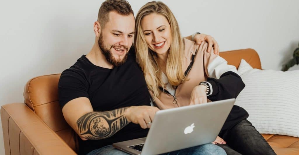 A couple looking at a laptop screen together on a couch.