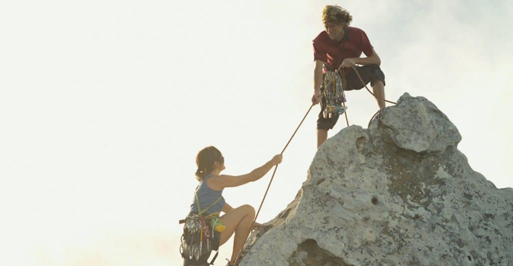 A man supporting his woman while she climbs a summit. 