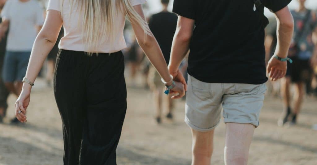 A man and a woman walking away from the camera, holding hands, with other blurred people in the background.