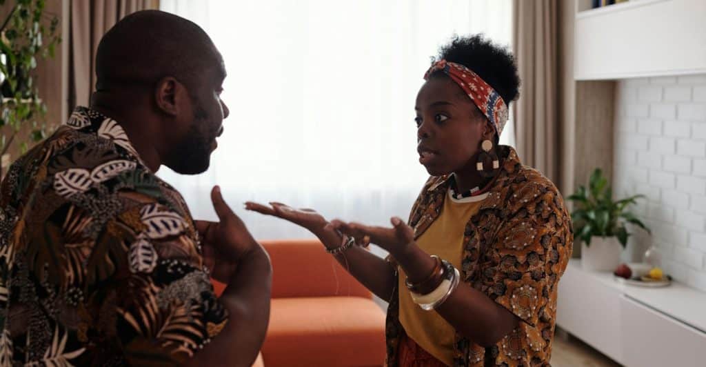 A man and a woman standing in a kitchen, facing each other and appearing to argue.