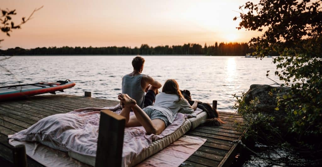 A couple and their dog are relaxing on a dock at sunset.