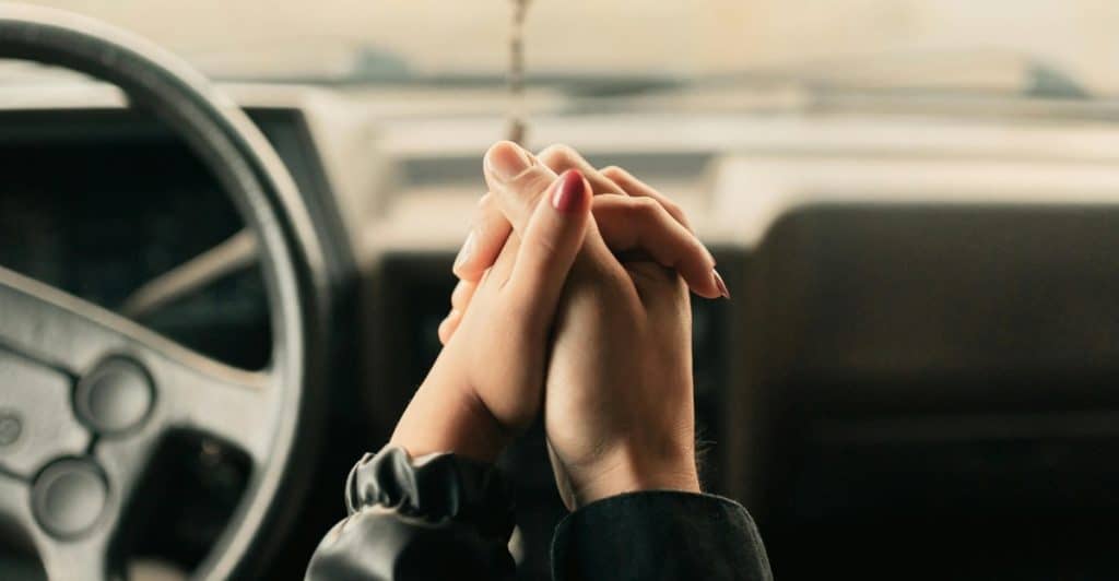 A close-up of a couple's hands clasped together inside a car